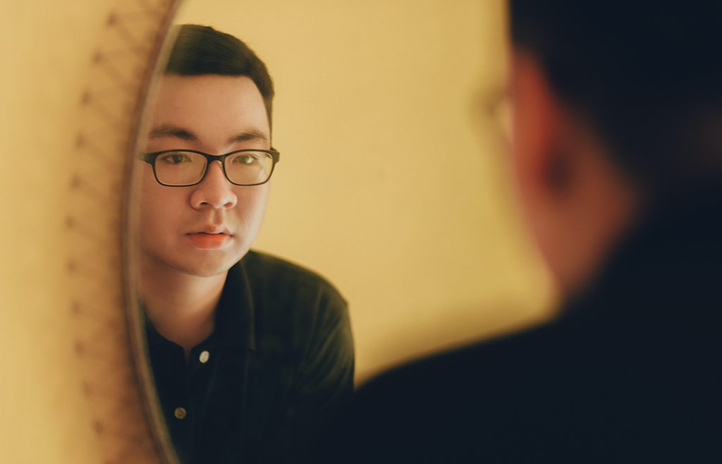 A man wearing glasses looks at himself in the mirror.