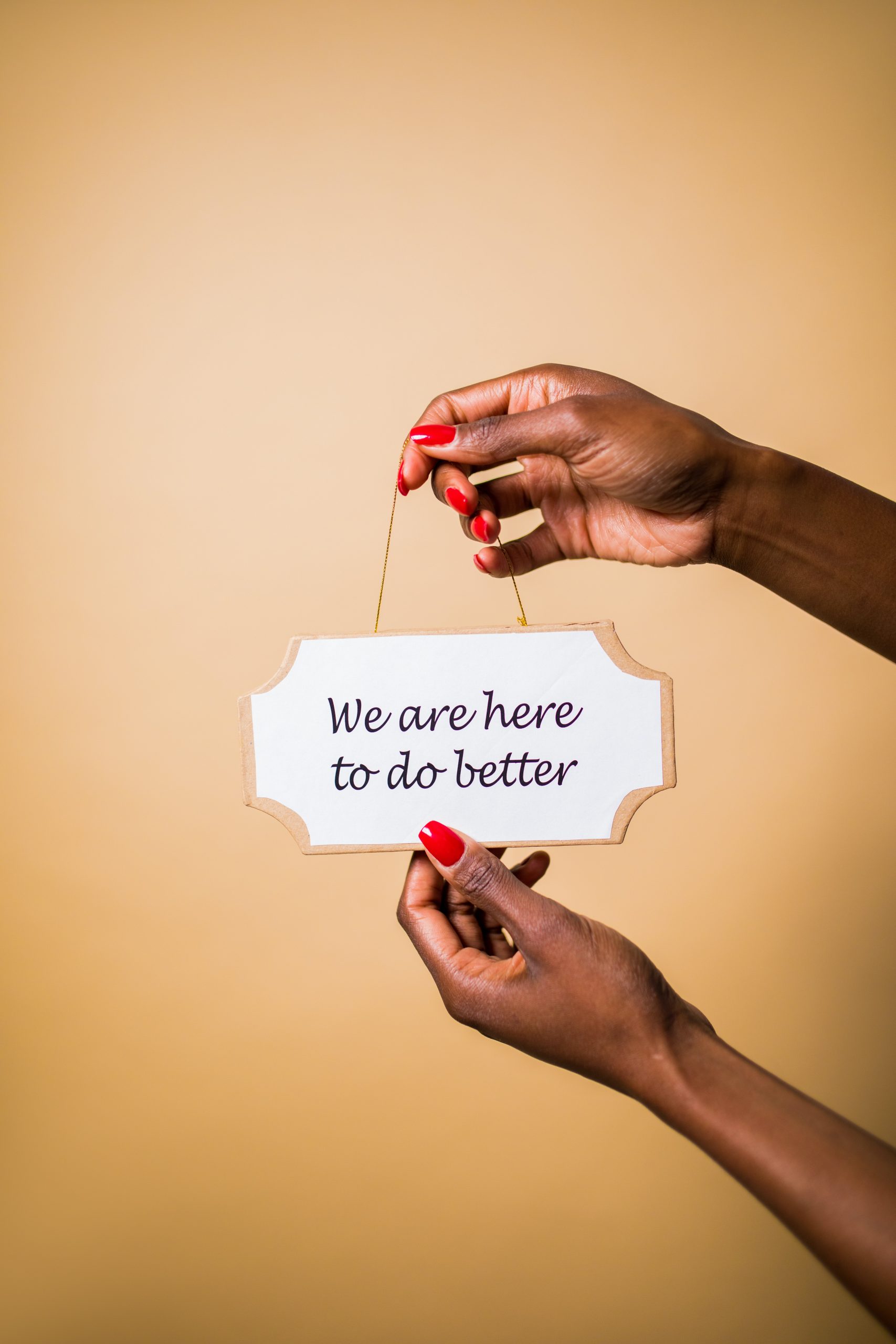 Hands holding sign that says "We are here to do better"